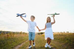 Running boy and girl holding two green and blue airplanes toy in the field during summer sunny day photo