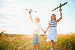Running boy and girl holding two green and blue airplanes toy in the field during summer sunny day photo