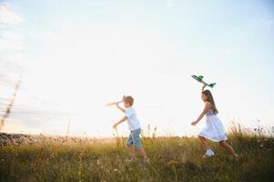 Running boy and girl holding two green and blue airplanes toy in the field during summer sunny day photo