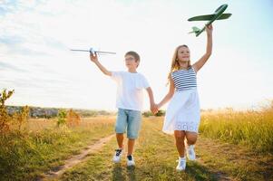 Running boy and girl holding two green and blue airplanes toy in the field during summer sunny day photo