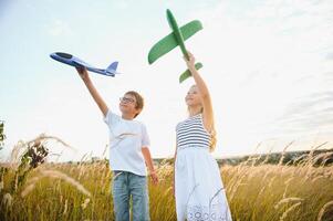 Running boy and girl holding two green and blue airplanes toy in the field during summer sunny day photo