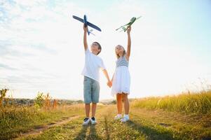 Running boy and girl holding two green and blue airplanes toy in the field during summer sunny day photo