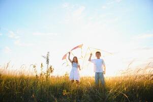 Happy children launch a kite in the field at sunset. Little boy and girl on summer vacation. photo