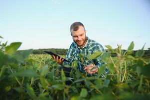 Young agronomist holds tablet touch pad computer in the soy field and examining crops before harvesting. Agribusiness concept. agricultural engineer standing in a soy field with a tablet in summer. photo