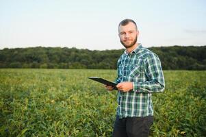 Young agronomist holds tablet touch pad computer in the soy field and examining crops before harvesting. Agribusiness concept. agricultural engineer standing in a soy field with a tablet in summer. photo