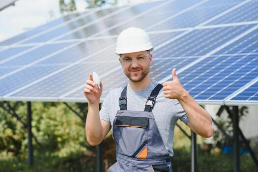 Technical expert in solar photovoltaic panels, remote control performs routine actions to monitor the system using clean renewable energy in the hand a light bulb. photo