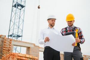 construcción ingenieros supervisando Progreso de construcción proyecto estar en nuevo hormigón piso parte superior techo y grua antecedentes. foto