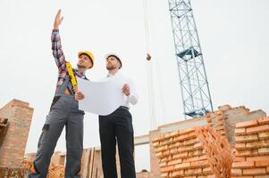 construcción ingenieros supervisando Progreso de construcción proyecto estar en nuevo hormigón piso parte superior techo y grua antecedentes. foto