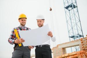 engineer and builder in hard hats discussing blueprint on construction site. photo