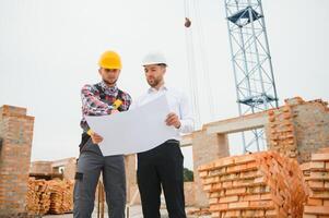 engineer and builder in hard hats discussing blueprint on construction site. photo