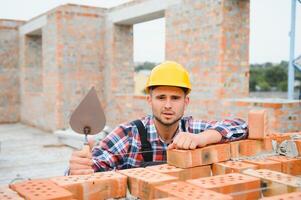 Using bricks. Young construction worker in uniform is busy at the unfinished building photo