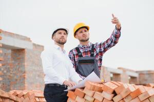 engineer and builder in hard hats discussing blueprint on construction site. photo