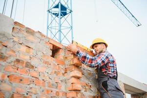 Using bricks. Young construction worker in uniform is busy at the unfinished building photo
