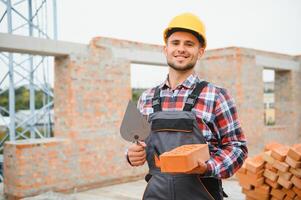 Using bricks. Young construction worker in uniform is busy at the unfinished building photo