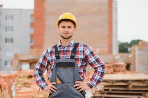 Construction worker man in work clothes and a construction helmet. Portrait of positive male builder in hardhat working at construction site. photo