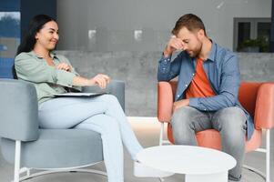 Handsome depressed man in casual clothes is leaning on his knees and telling about his problems while sitting on the couch at the psychotherapist. photo