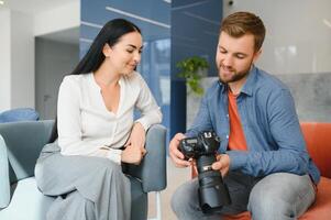 Photographer in office shows photo model in camera. Consultant adjusts activities company as whole. Photo session employees in workplace. Manager well-executed project. Photos best employees company.