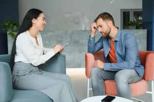 Handsome depressed man in casual clothes is leaning on his knees and telling about his problems while sitting on the couch at the psychotherapist. photo