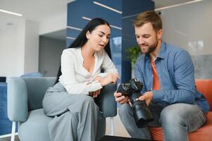 Photographer in office shows photo model in camera. Consultant adjusts activities company as whole. Photo session employees in workplace. Manager well-executed project. Photos best employees company.