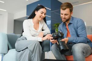 Young photographer man in blue shirt watching photo with client woman after photo session and smiling and looking at each other