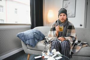 Young man suffering from a common cold and flu or allergy sit at home wrapped in blanket and wipe his nose with tissues while he have a strong headache pain, healthcare concept. photo