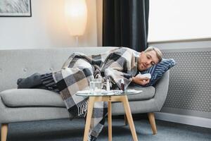 A sick man sits at home on a gray sofa with a blanket. Illness, protection, coronavirus, illness, flu photo