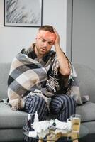 A sick man sits at home on a gray sofa with a blanket. Illness, protection, coronavirus, illness, flu photo