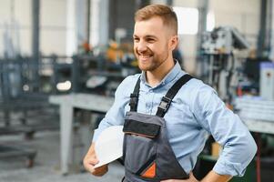 Portrait of factory worker in protective uniform and hardhat standing by industrial machine at production line. People working in industry photo