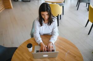 Smiling girl student study online with skype teacher, happy young woman learn language listen lecture watch webinar write notes look at laptop sit in cafe, distant education photo