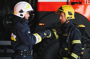 Two firefighters in protective clothing in helmets with fire engine, friendly handshake photo