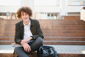 University.Smiling young student man holding a book and a bag on a university background .Young smiling student outdoors Life style.City.Student. photo