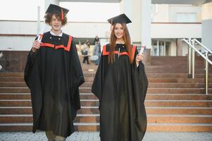 Happy friends on graduation day. Portrait of two cheerful joyful students standing near university building. photo
