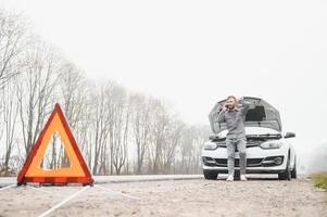Man use a cellphone call garage in front of the open hood of a broken car on the road in the forest. Car breakdown concept. photo