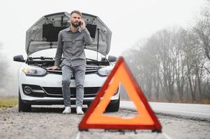 Man use a cellphone call garage in front of the open hood of a broken car on the road in the forest. Car breakdown concept. photo