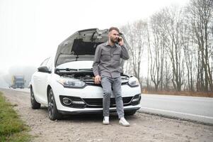 Man use a cellphone call garage in front of the open hood of a broken car on the road in the forest. Car breakdown concept. photo