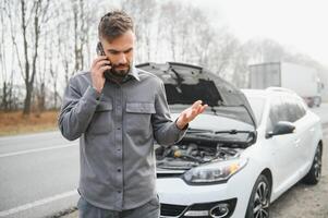 Man use a cellphone call garage in front of the open hood of a broken car on the road in the forest. Car breakdown concept. photo