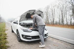 young stressed man having trouble with his broken car looking in frustration at failed engine photo