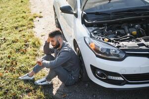 Man use a cellphone call garage in front of the open hood of a broken car on the road in the forest. Car breakdown concept. photo