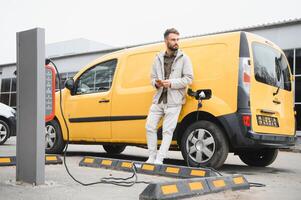 Casual man near electric car waiting for the finish of the battery charging process photo