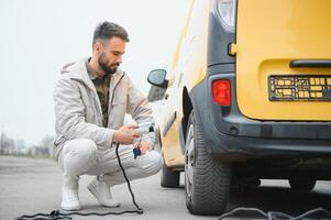 Man Holding Power Charging Cable For Electric Car In Outdoor Car Park. And he s going to connect the car to the charging station in the parking lot near the shopping center photo
