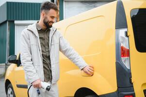 Man Holding Power Charging Cable For Electric Car In Outdoor Car Park. And he s going to connect the car to the charging station in the parking lot near the shopping center photo