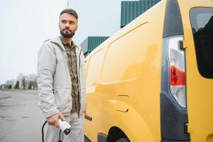 Portrait of a young man standing with charging cable near the charging station photo