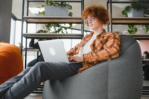 Portrait of Caucasian male freelancer in trendy apparel sitting at cafeteria table and doing remote work for programming design of public website, skilled software developer posing in coworking space. photo