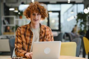 Cheerful male freelancer browsing funny content while networking in social media using netbook technology in street cafe, happy hipster guy enjoying free time for online blogging via laptop photo