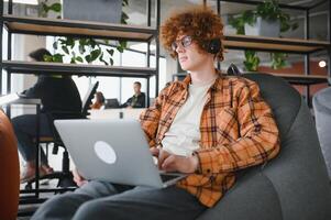 Portrait of Caucasian male freelancer in trendy apparel sitting at cafeteria table and doing remote work for programming design of public website, skilled software developer posing in coworking space. photo