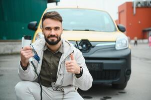 Stylish man inserts the charging cable into the socket of electric car photo