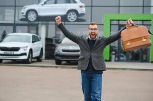 Happy buyer near the car in front of the modern avtosalon building photo