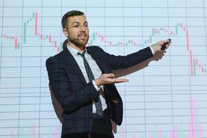 Man is standing near projector and showing graphs and business graphs. photo
