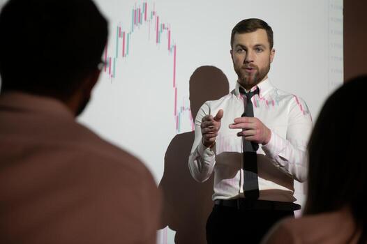Man is standing near projector and showing graphs and business graphs. photo