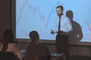 Man is standing near projector and showing graphs and business graphs. photo